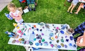 Girl painting rocks on table filled with colorful painted rocks