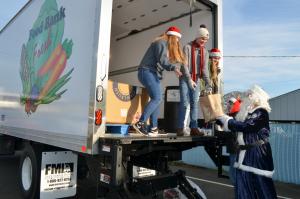 Santa in a blue suit hands canned food up to volunteers loading a semi-truck for the Food Bank. 