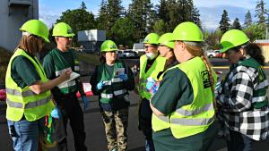 St. Helens CERT members huddle in a group with hard hats and vests on to talk about a simulated disaster situation. 
